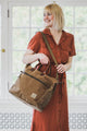 Woman in a rust-colored dress holding a brown bag indoors.