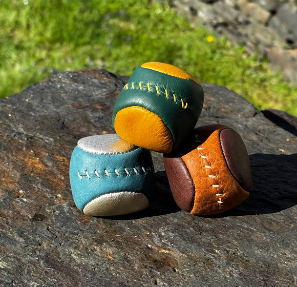 Three leather shoes in green, brown, and blue on a stone surface with grass in the background.