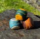 Three leather shoes in green, brown, and blue on a stone surface with grass in the background.