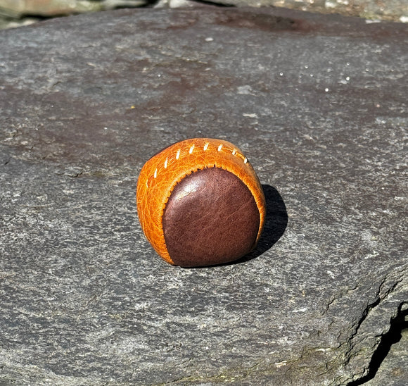 A small, round footbag made from 2 panels of tan and brown leather.
