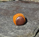 A small, round footbag made from 2 panels of tan and brown leather.